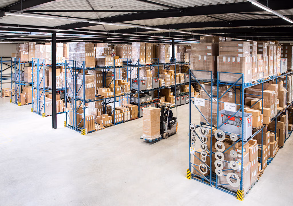 Een magazijn met hoge rekken vol dozen, pakjes en haardaccessoires; een vorkheftruck verplaatst de goederen efficiënt in de ruime, goed verlichte ruimte.