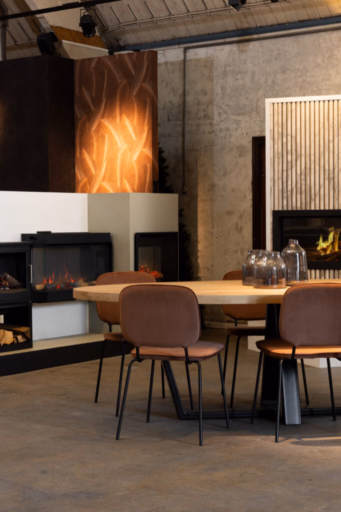 Een moderne eethoek met een ronde houten tafel, bruin gestoffeerde stoelen en glazen vazen. Op de achtergrond zijn open haarden versierd met stijlvolle haardaccessoires, gestructureerde muren en warme sfeerverlichting.