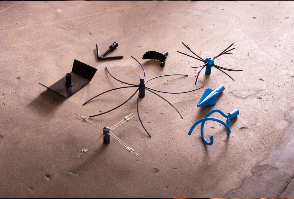 Zes verschillende wied- en cultivatiehulpstukken van Haardaccessoires staan op een betonnen oppervlak. Ze variëren in vorm, sommige hebben metalen tanden, bladen of gebogen armen, meestal in zwarte of blauwe tinten.