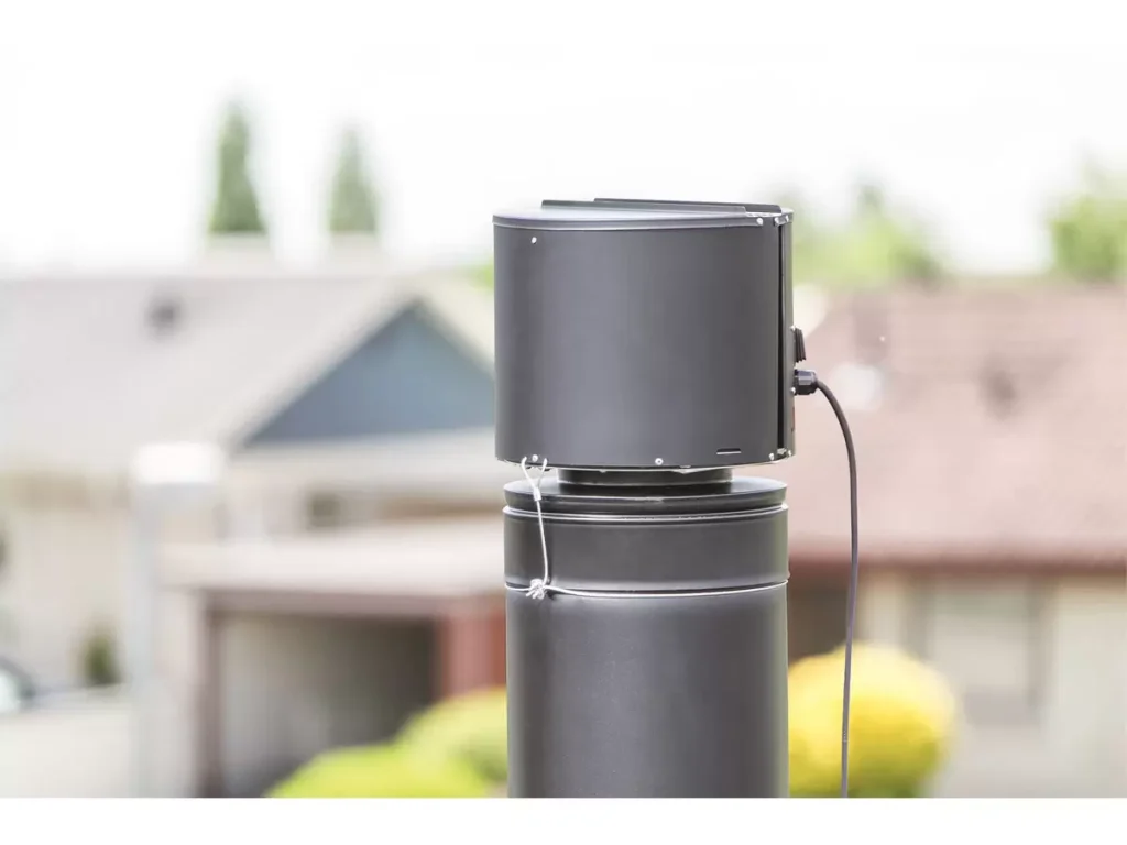 A close-up of a cylindrical weather sensor mounted on a pole outdoors, with houses and greenery blurred in the background, showcases advanced monitoring solutions by IHS Group.
