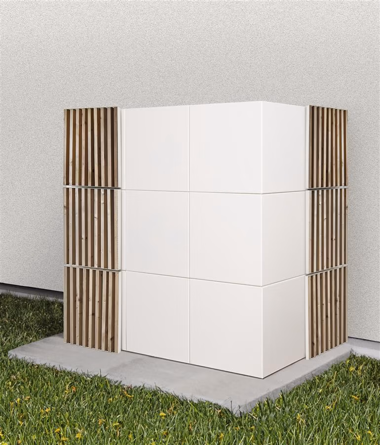 Un moderno contenitore da esterno a forma di scatola, di colore bianco, con doghe verticali in legno agli angoli, posizionato su una lastra di cemento accanto a un muro bianco e circondato da erba, perfetto per organizzare con stile gli accessori per capelli all'ingrosso.
