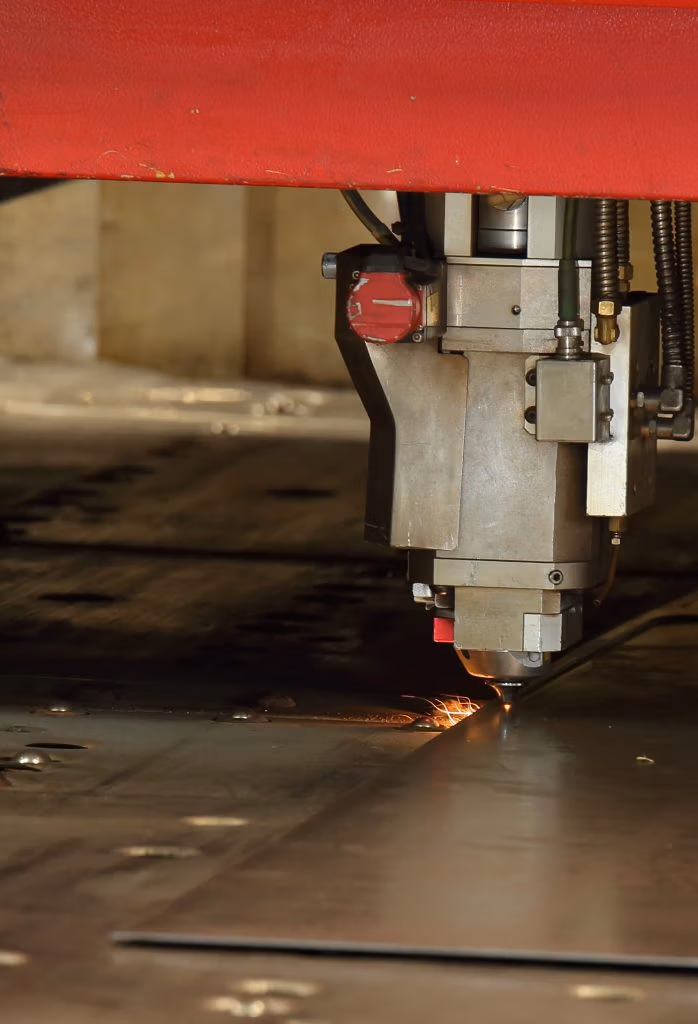 Close-up van een CNC lasersnijmachine die precies door een plaat metaal snijdt, met zichtbare vonken op het contactpunt.