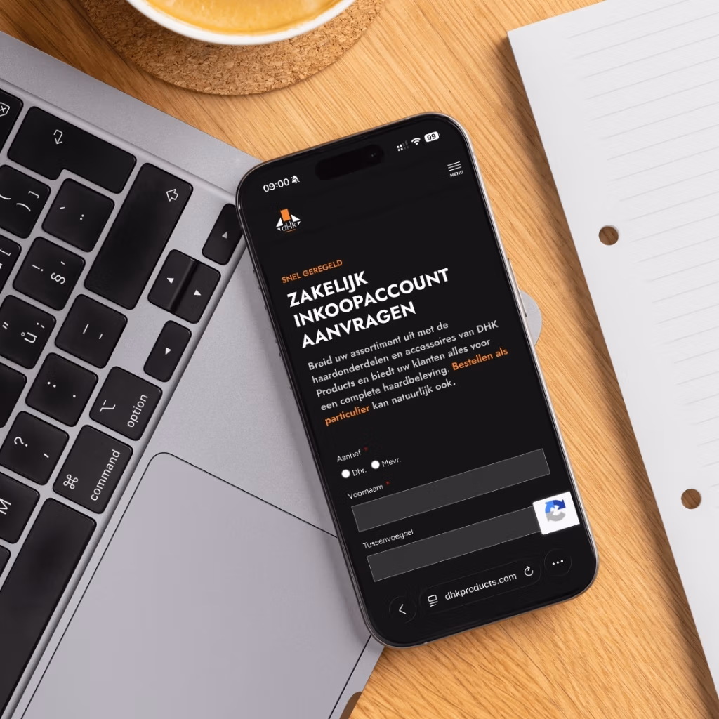 Een smartphone met een aanvraagformulier voor een Nederlandse zakelijke inkooprekening ligt op een houten bureau naast een laptoptoetsenbord, notitieblok en koffiekopje - ideaal voor ondernemers die de dropshipping-mogelijkheden van haardaccessoires onderzoeken.